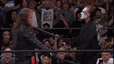 two men are wrestling in a ring with a crowd watching and a sign that says aew on it .