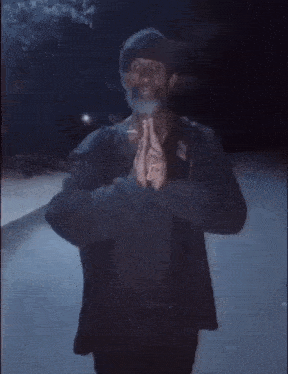 a man with a beard is standing in the dark with his hands together in a prayer position .