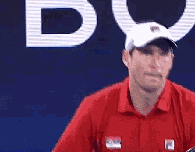 a man wearing a red shirt and a white hat is standing in front of a blue background .