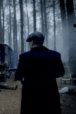 a man in a black coat and hat stands in a dark forest
