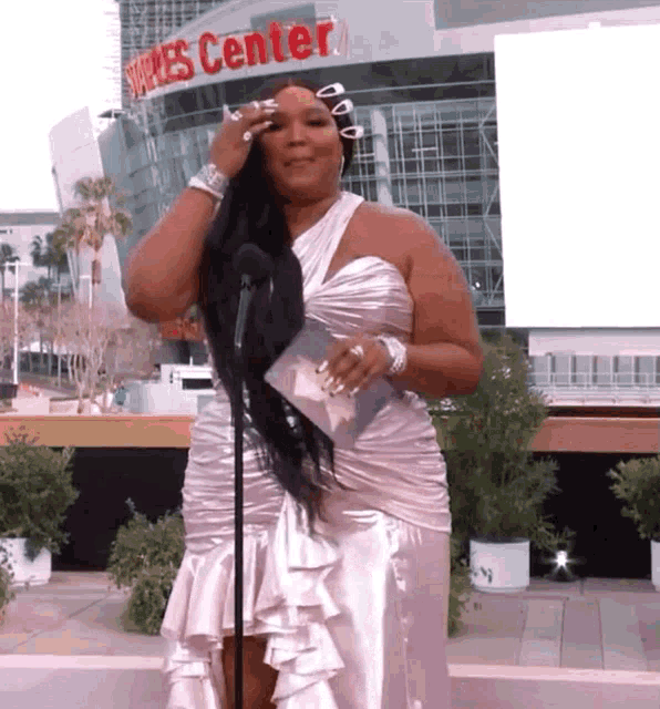 a woman in a white dress stands in front of a microphone in front of a building that says shakes center