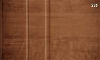 a woman is standing in front of a wooden wall and making a surprised face .