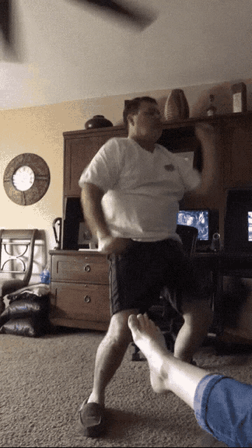 a man in a white shirt is dancing in a living room with a clock on the wall
