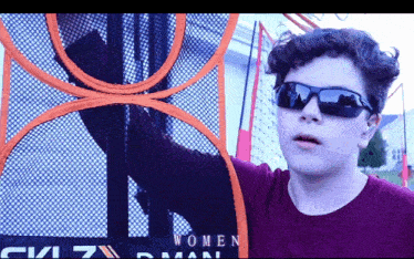 a boy wearing sunglasses is standing in front of a basketball net that says women on it