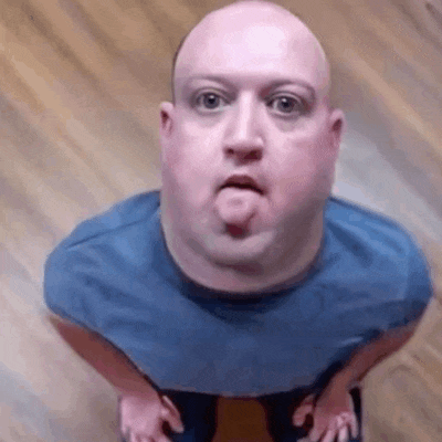 a bald man in a blue shirt is sticking his tongue out while standing on a wooden floor .