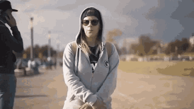 a woman wearing a hoodie and sunglasses is standing in front of a man talking on a cell phone .