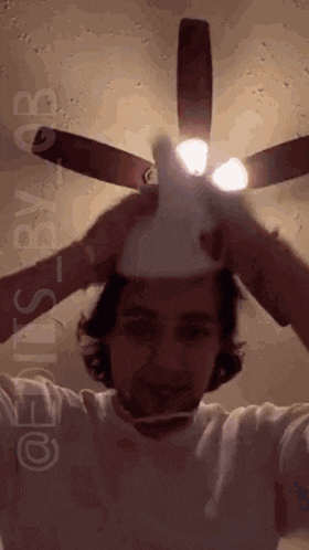 a man in a white shirt is holding a light bulb in front of a ceiling fan ..