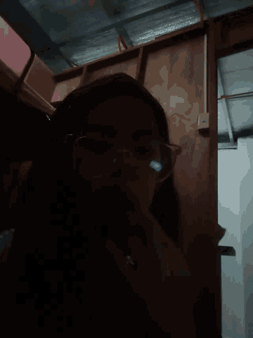 a woman wearing glasses looks down at something in a dark room