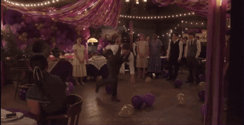 a group of people are dancing in a room with purple balloons