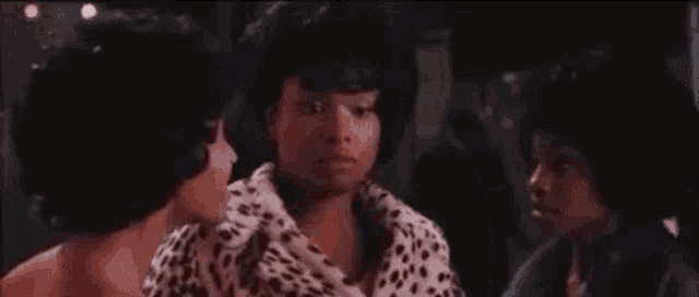 a woman in a leopard print jacket is talking to two other women in a room .