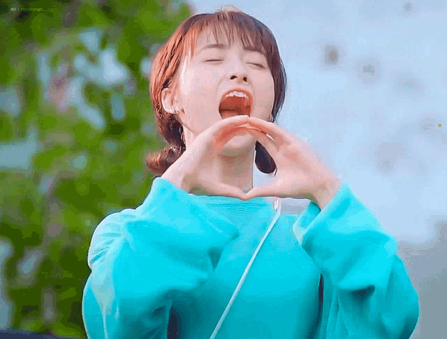 a woman in a blue shirt is making a heart with her hands