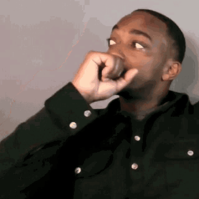 a man in a black shirt is covering his mouth with his hand and looking away .