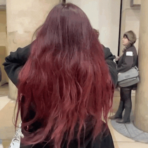 a woman with long red hair is standing in front of a woman with a purse