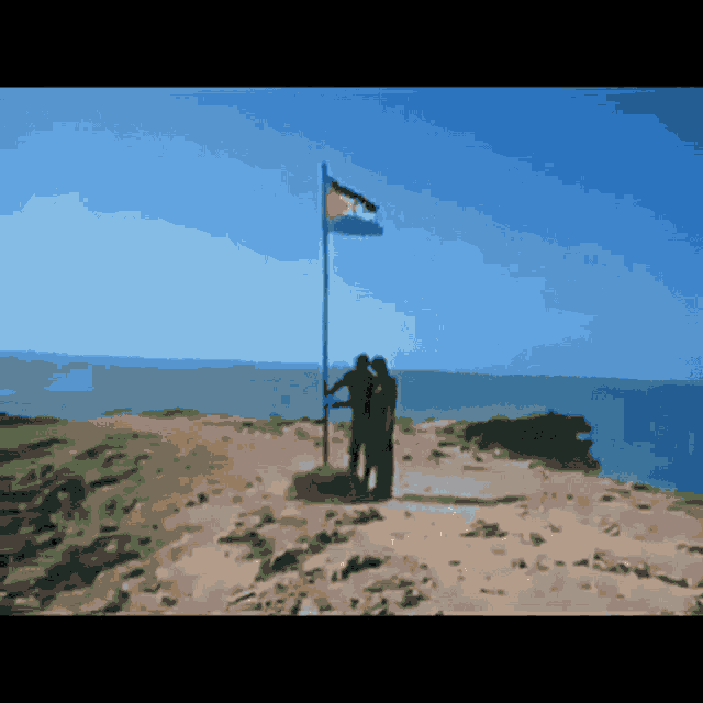 a couple standing on top of a sandy hill with a flag in the background