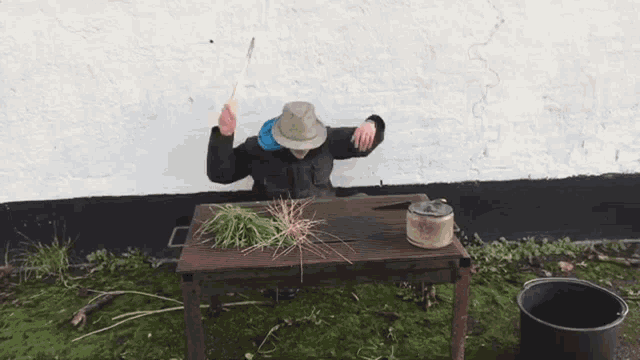 a man sitting at a table with his arms in the air holding a stick