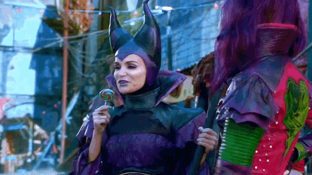 a woman dressed as maleficent is holding a lollipop and talking to another woman .