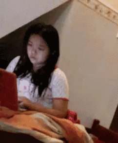 a young girl is sitting on a bed using a laptop
