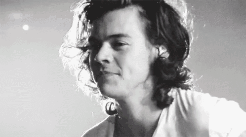 harry styles is wearing a white shirt and has long hair in a black and white photo .