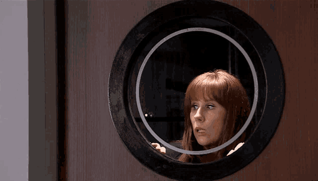 a woman looking through a round window on a door