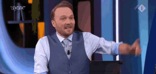 a man in a blue vest and white shirt stands in front of a tv screen that says vpro