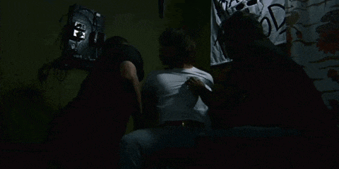 a group of men are standing around a man in a dark room .