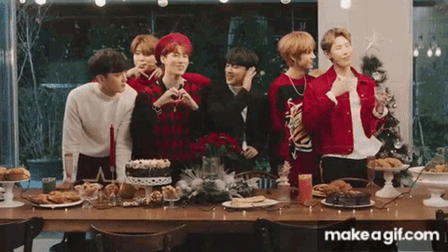 a group of young men are standing around a table with food and a cake .