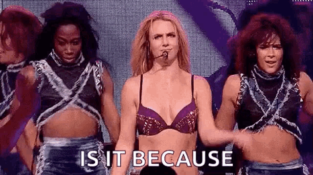 a woman in a bra is standing in front of a group of dancers on a stage and says `` is it because '' .