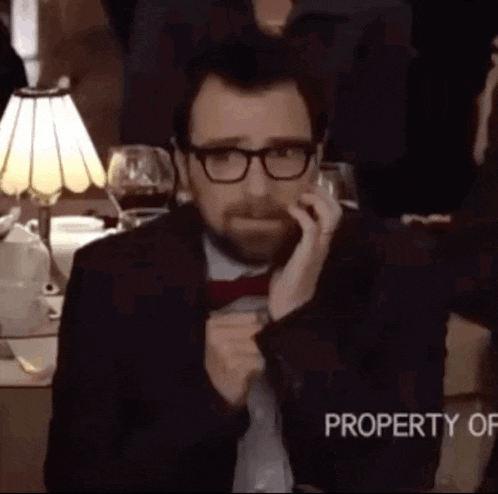 a man wearing glasses and a red bow tie is sitting at a table with a lamp and a property of sign