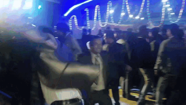 a crowd of people are dancing in a dark room with a blue light behind them