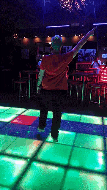 a man in a red shirt is dancing on a dance floor with green lights