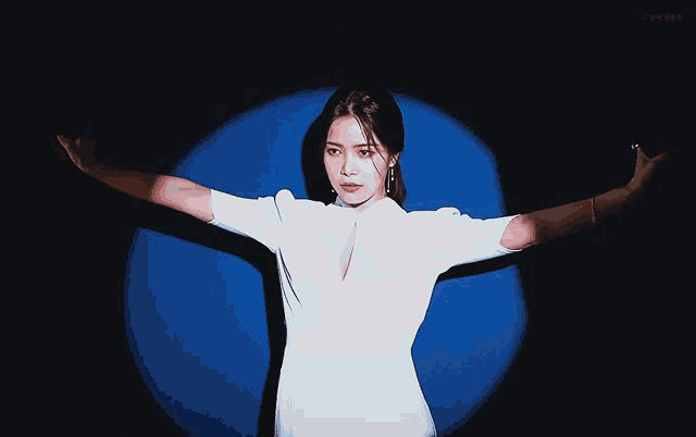 a woman in a white dress is standing in front of a blue circle with her arms outstretched