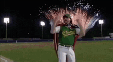 a baseball player in a green jersey is standing on a field with fireworks in the background .
