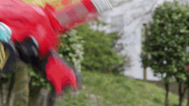 a blurred image of a red and yellow toy car in a garden