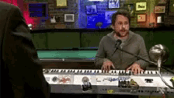 a man is playing a keyboard in front of a microphone and a pool table