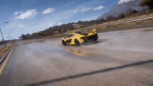 a yellow sports car is driving down a road with a mountain in the background