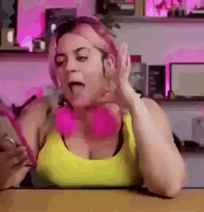 a woman with pink hair is sitting at a table wearing headphones and a yellow shirt .