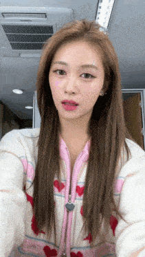 a woman wearing a pink and white jacket with hearts on it is taking a selfie