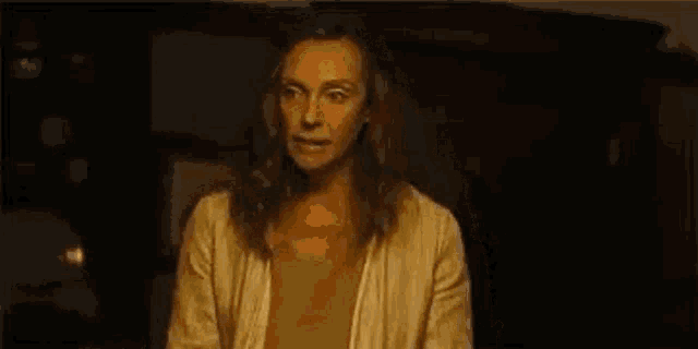 a woman is standing in a dark room with her hands up in the air and a surprised look on her face .