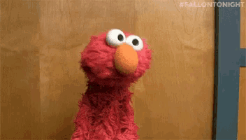 elmo the sesame street character is standing in front of a wooden wall .