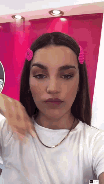 a woman wearing a white shirt and a pink hair clip is taking a selfie
