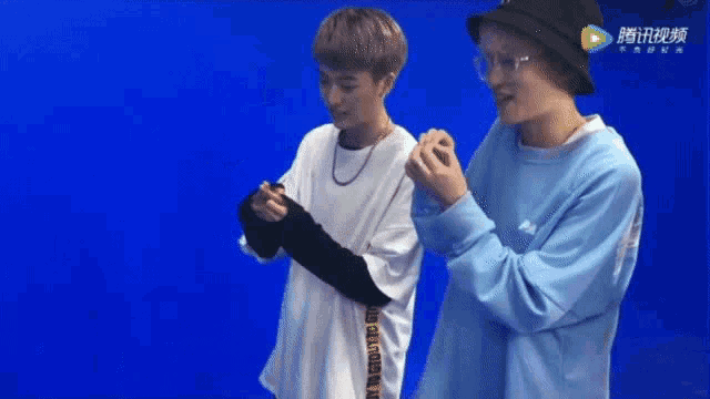 two young men are standing next to each other in front of a blue screen with chinese writing on it .