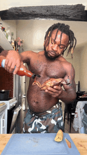 a shirtless man with dreadlocks is pouring hot sauce on a piece of meat