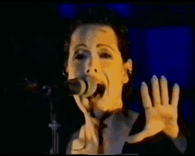 a woman is singing into a microphone with her hands outstretched
