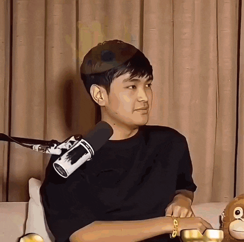 a man is sitting on a couch in front of a microphone and a stuffed animal .