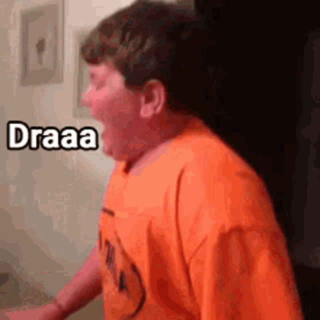 a young boy in an orange shirt is standing in a room with his mouth open .