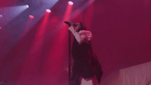 a woman is singing into a microphone on a stage with red smoke coming out of the ceiling .
