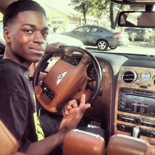 a young man sitting in a bentley giving the middle finger