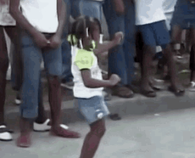 a little girl is dancing in front of a crowd of people on the street .