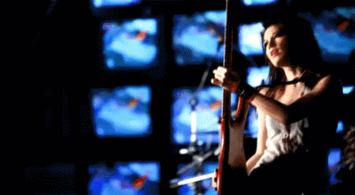 a woman playing a guitar in front of a wall of monitors
