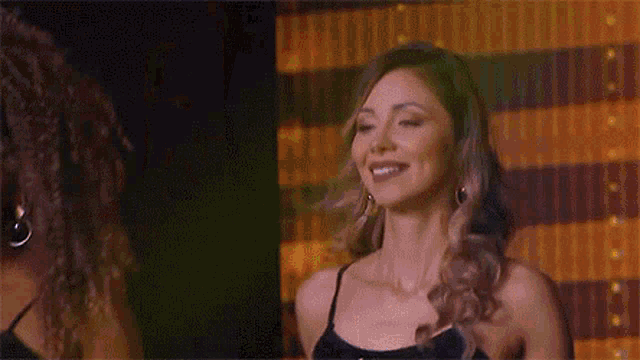 a woman in a black dress is smiling and looking at the camera .